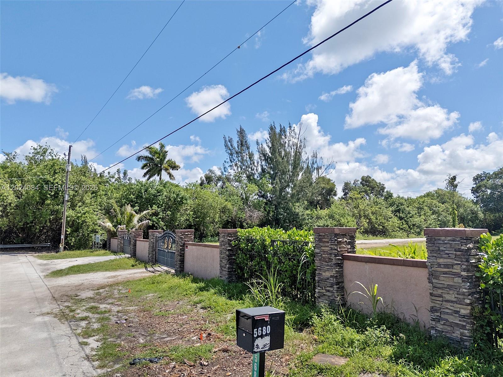 A stone and stucco wall with a metal gate borders a lot with vegetation — 5680 Pinetree Rd, Parkland FL 33067, PARKLAND, FL