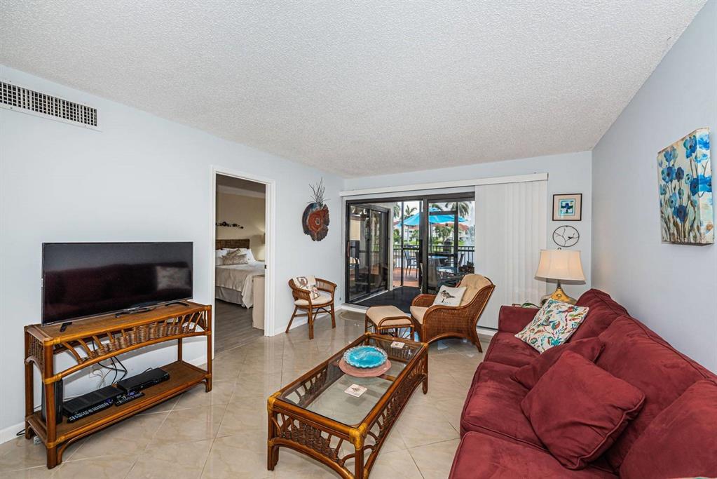 A living room features a red sofa, rattan furniture, tile floors, and a sliding glass door — 6294 BAHIA DEL MAR CIRCLE UNIT 114, ST PETERSBURG, FL