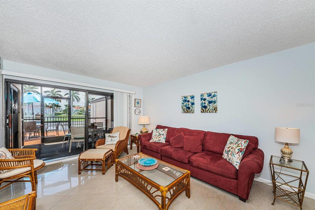 A living room features a red sofa, wicker coffee table, and a sliding glass door — 6294 BAHIA DEL MAR CIRCLE UNIT 114, ST PETERSBURG, FL