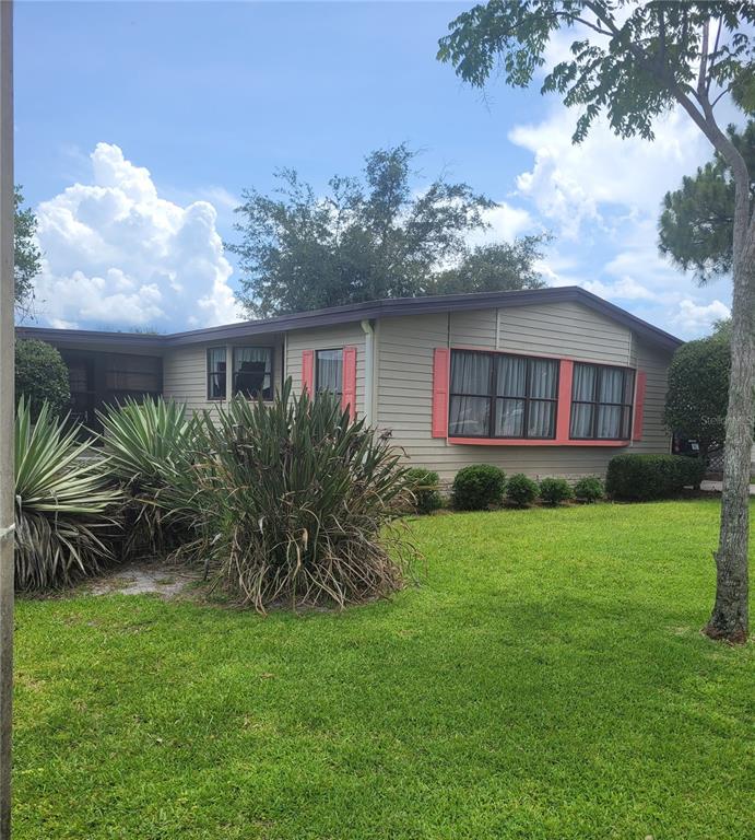 A single-story manufactured home with beige siding, coral shutters, and a landscaped front yard — 3211 WEKIVA ROAD, TAVARES, FL
