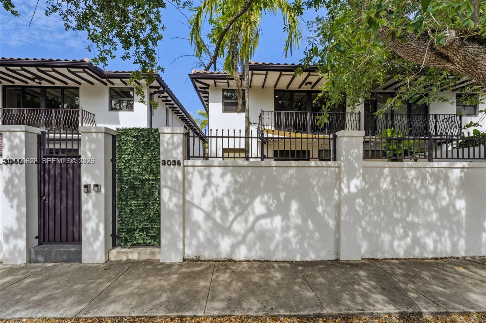 A white stucco building with a black metal fence and gate stands behind a sidewalk — 3036 Mcdonald Street, Miami FL 33133, MIAMI, FL