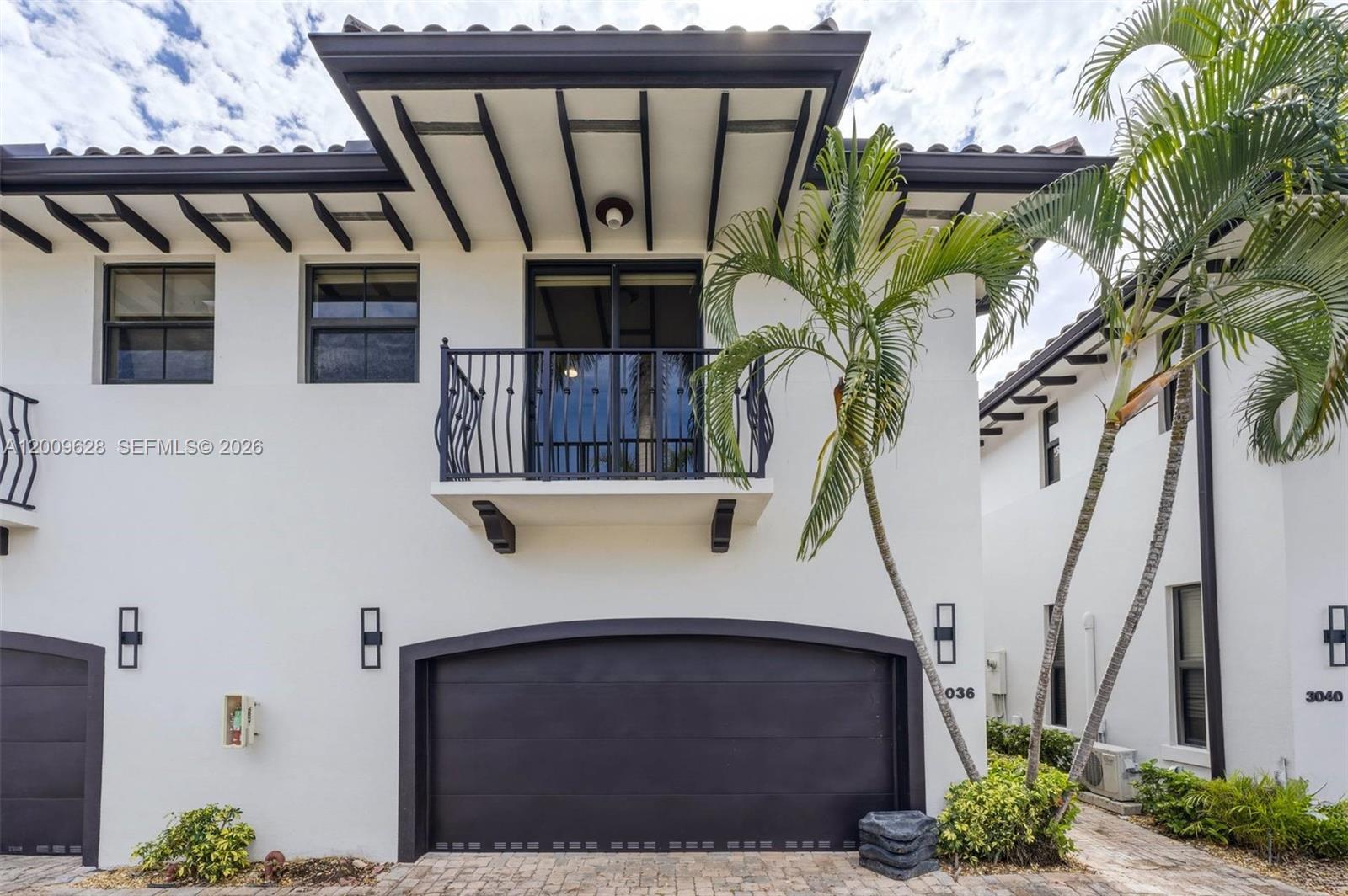 The exterior of a two-story white townhouse features a dark garage door and balcony — 3036 Mcdonald Street, Miami FL 33133, MIAMI, FL