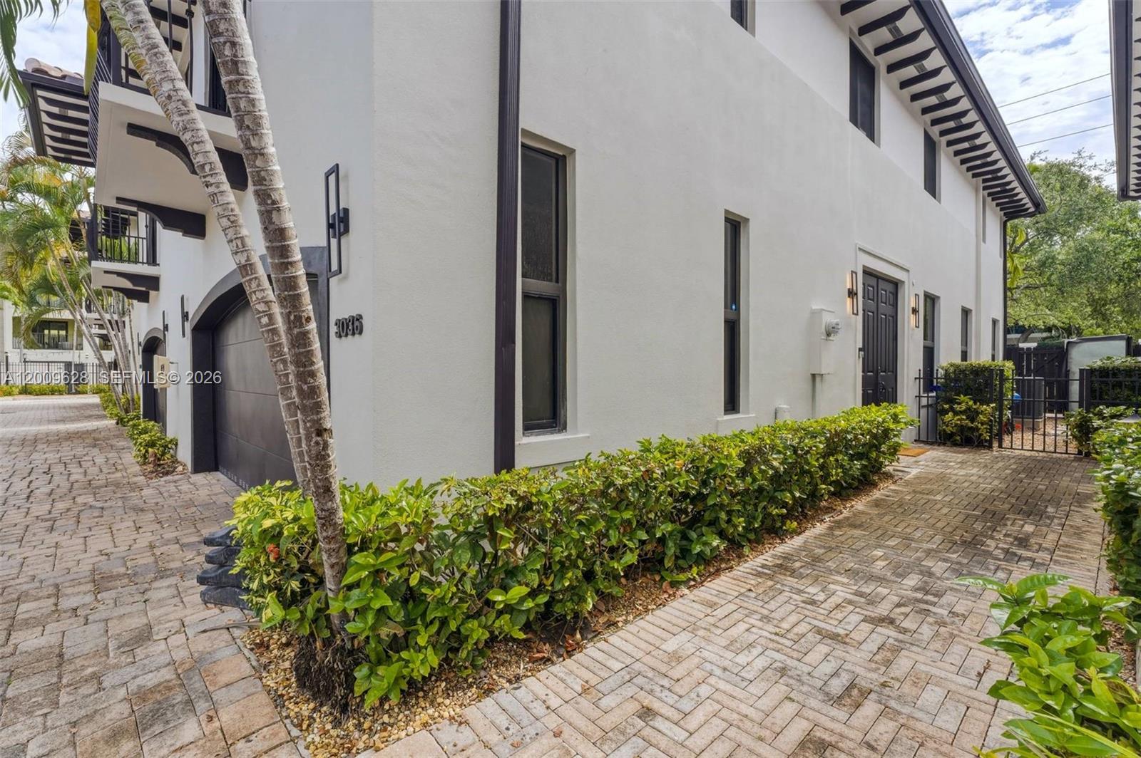 A white two-story house exterior features a dark garage door, brick driveway, and landscaping — 3036 Mcdonald Street, Miami FL 33133, MIAMI, FL