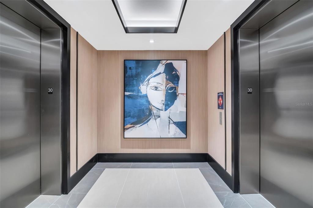 An elevator lobby features two stainless steel doors, wood-paneled walls, and a large abstract painting — 275 1ST AVENUE S UNIT 2807, ST PETERSBURG, FL
