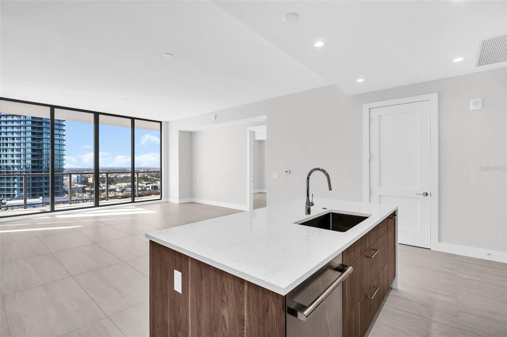 A modern kitchen island with a sink sits before a bright living area with floor-to-ceiling windows — 275 1ST AVENUE S UNIT 2807, ST PETERSBURG, FL