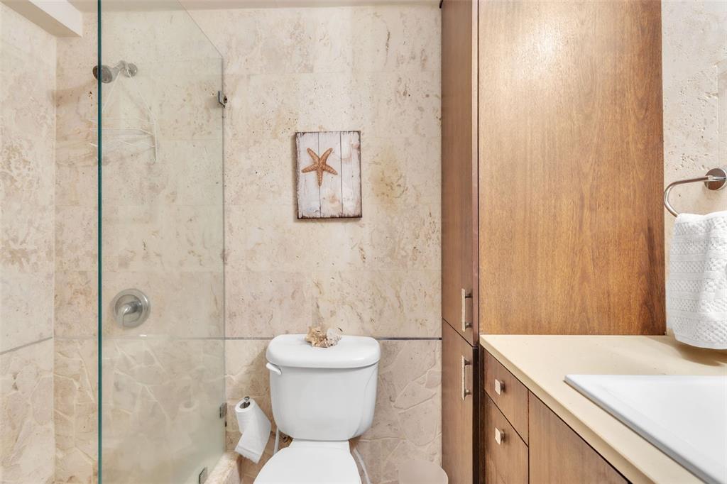 A bathroom features a glass-enclosed shower, a white toilet, and wood cabinetry with stone walls — 7 ISLA SAN MARCOS UNIT 7, HUMACAO, PR