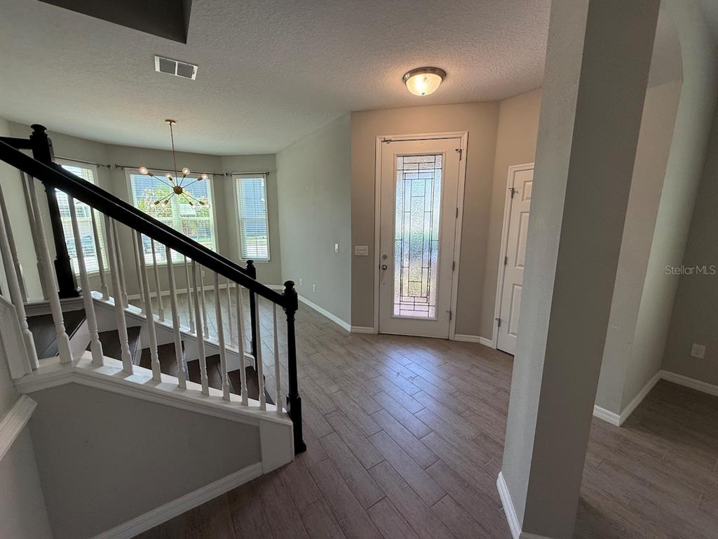 An entryway features wood-look tile flooring, a staircase with a black railing, and a front door — 5251 VILLA ROSA AVENUE, ST CLOUD, FL