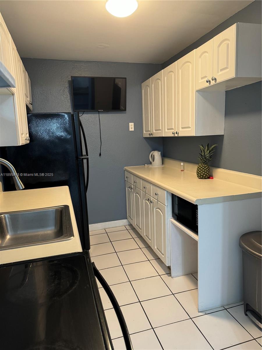 A kitchen features white cabinets, a black refrigerator, a stainless steel sink, and tiled flooring — 1251 NE 108th St # 602, Miami FL 33161, MIAMI, FL