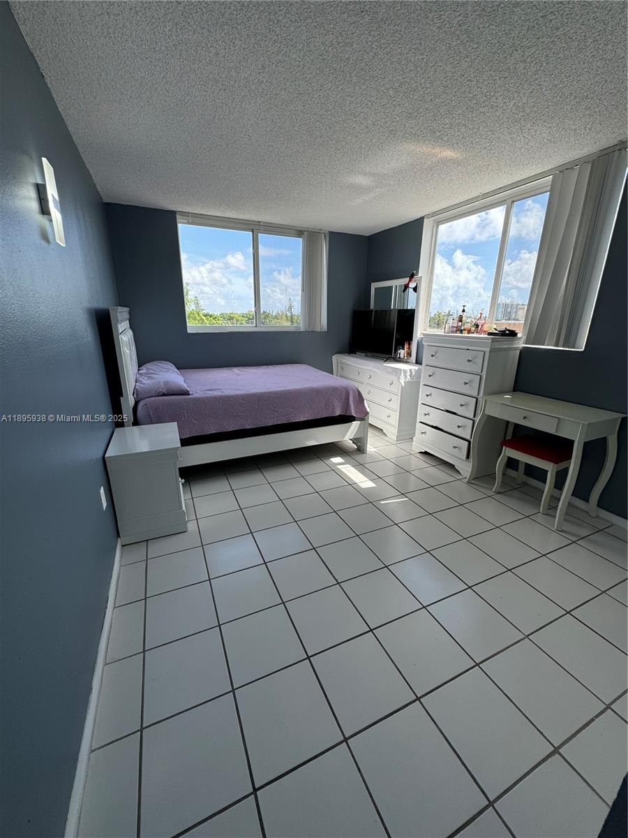 A bedroom with blue walls, white tile floors, a bed, and a white dresser — 1251 NE 108th St # 602, Miami FL 33161, MIAMI, FL