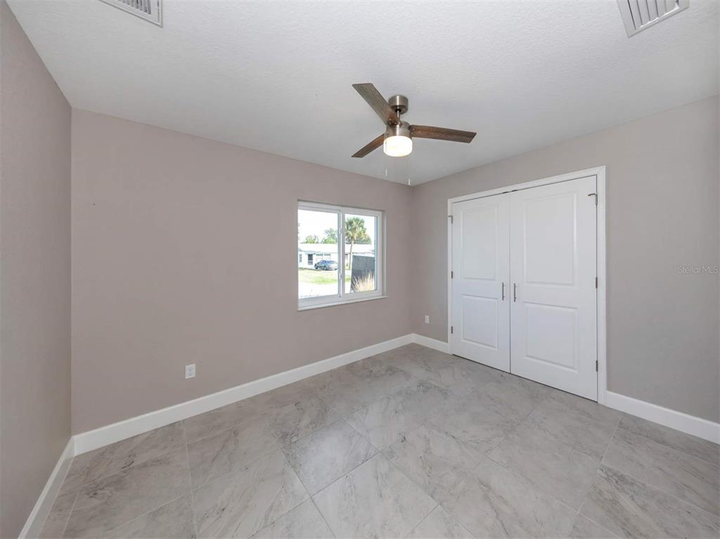 A bedroom with light gray walls, tile flooring, a ceiling fan, and white closet doors — 125 BOUNDARY BOULEVARD UNIT 2, ROTONDA WEST, FL