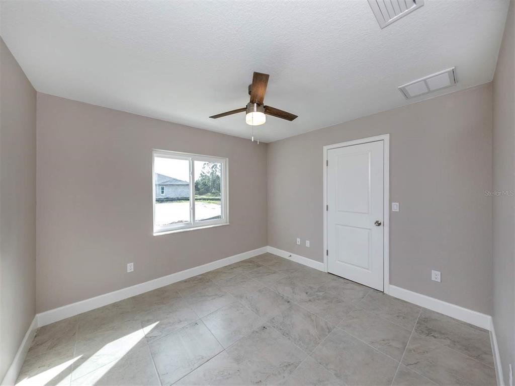 An empty room features light gray walls, tile flooring, a ceiling fan, and a white door — 125 BOUNDARY BOULEVARD UNIT 2, ROTONDA WEST, FL
