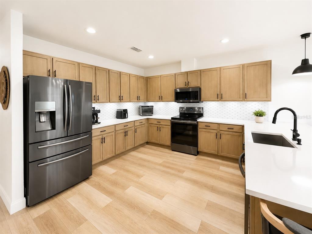 A kitchen features light wood cabinets, stainless steel appliances, white countertops, and light wood flooring — 5267 WHITE EGRET LANE, LAKELAND, FL