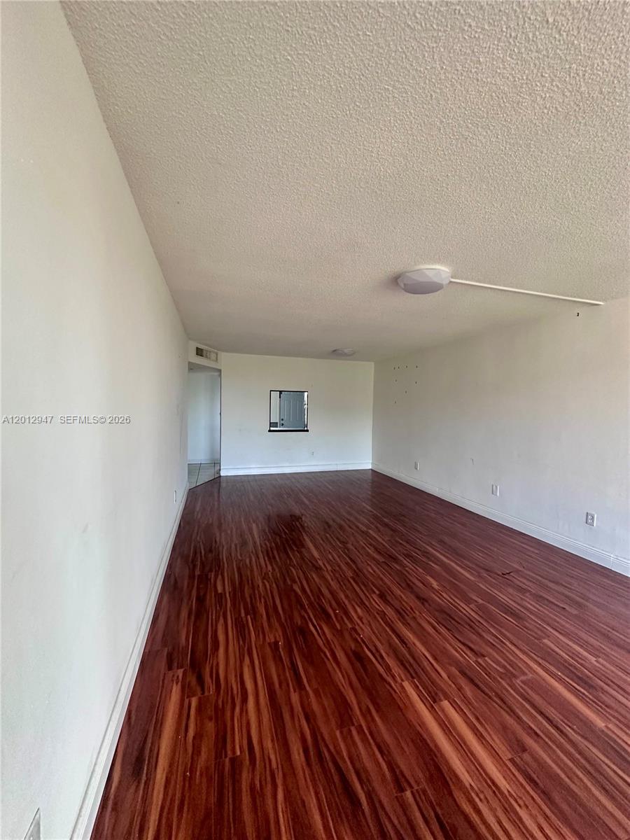 An empty room features white walls, a textured ceiling, and dark wood-look flooring — 1501 NE 191st St # C412, Miami FL 33179, MIAMI, FL