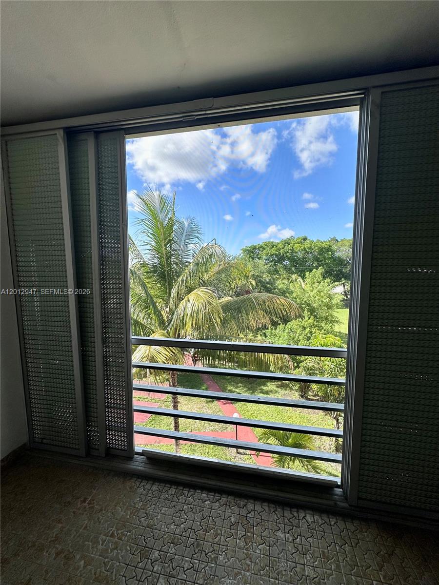 A view of a palm tree and green space through a screened balcony window — 1501 NE 191st St # C412, Miami FL 33179, MIAMI, FL