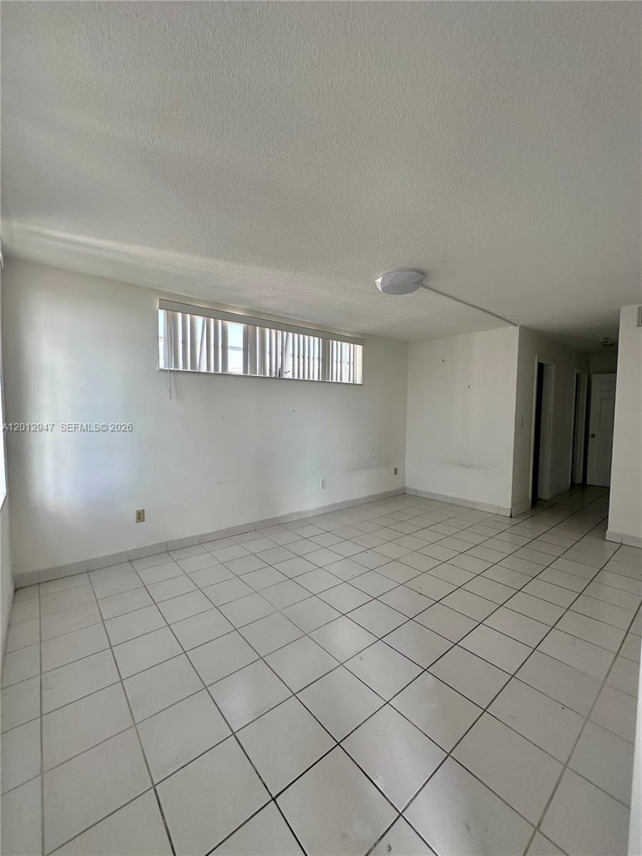 An empty room features white tiled floors, white walls, and a horizontal window with blinds — 1501 NE 191st St # C412, Miami FL 33179, MIAMI, FL