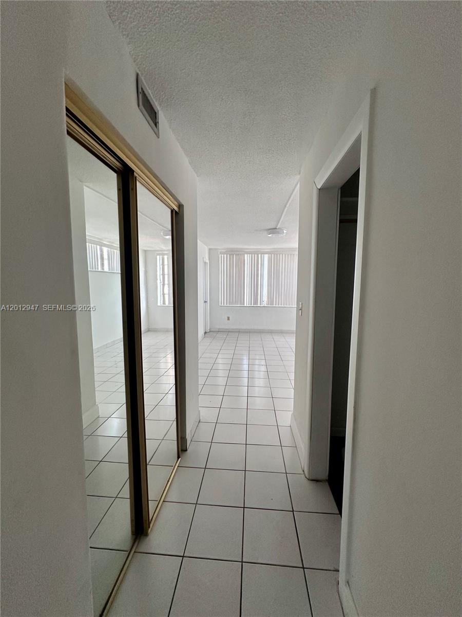 A hallway with white tiled floors leads to a room with large windows — 1501 NE 191st St # C412, Miami FL 33179, MIAMI, FL