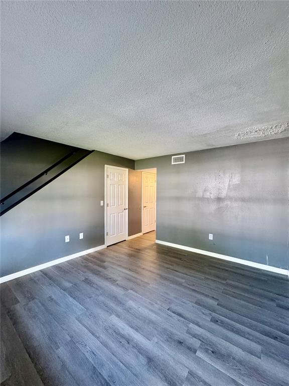 An empty room features gray walls, wood-look flooring, and a staircase with a black railing — 1415 RIDGE LAKE COURT, LAKELAND, FL