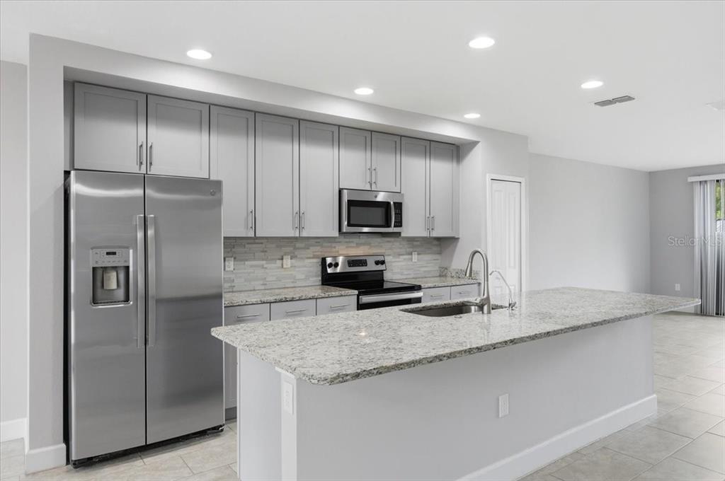 A modern kitchen features gray cabinets, stainless steel appliances, and a granite-topped island — 4712 TERRA ESMERALDA DRIVE, KISSIMMEE, FL