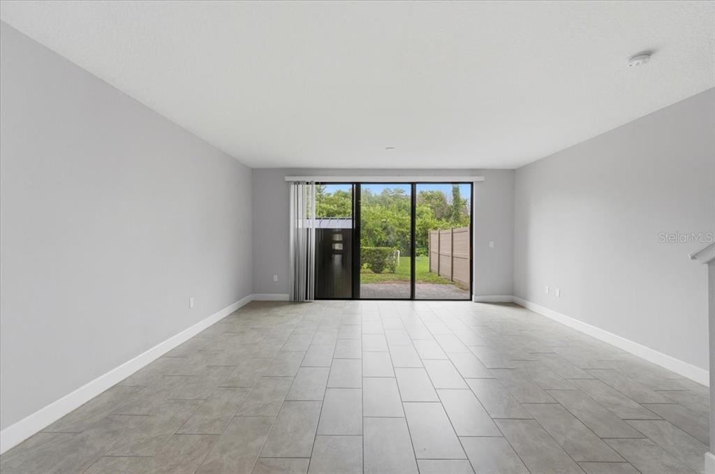 An empty living room features light gray walls, large floor tiles, and a sliding glass door — 4712 TERRA ESMERALDA DRIVE, KISSIMMEE, FL
