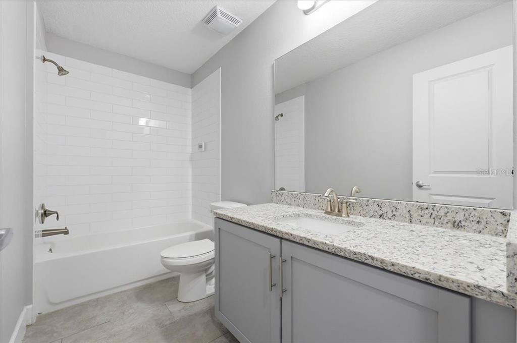 A bathroom features a gray vanity with a granite countertop, a toilet, and a tub-shower — 4712 TERRA ESMERALDA DRIVE, KISSIMMEE, FL