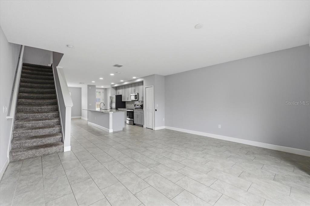 An open-concept living area features gray tile flooring, a carpeted staircase, and a modern kitchen — 4712 TERRA ESMERALDA DRIVE, KISSIMMEE, FL