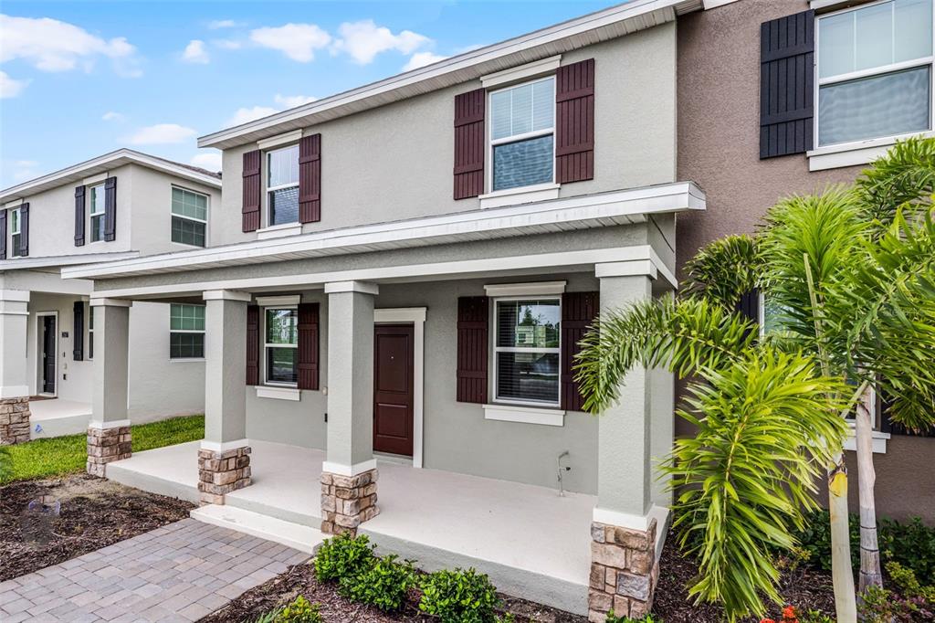 A two-story house exterior features a covered front porch with stone-based columns and shutters — 2563 RELAXING LANE, KISSIMMEE, FL