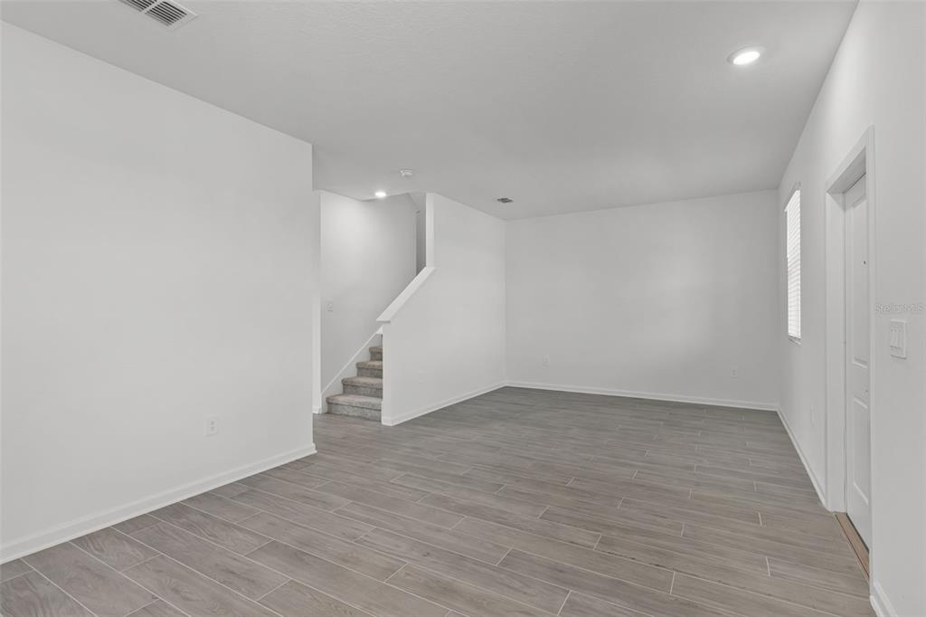An empty room with gray wood-look tile flooring, white walls, and a carpeted staircase — 2563 RELAXING LANE, KISSIMMEE, FL