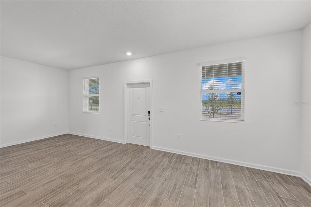 An empty room features white walls, light wood-look flooring, two windows, and a door — 2563 RELAXING LANE, KISSIMMEE, FL