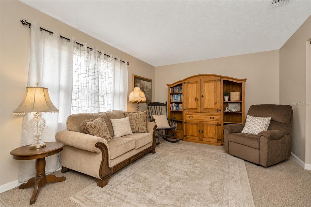 A living room features a beige sofa, a brown recliner, and a wooden entertainment center — 12212 FLORAL LANE, THONOTOSASSA, FL