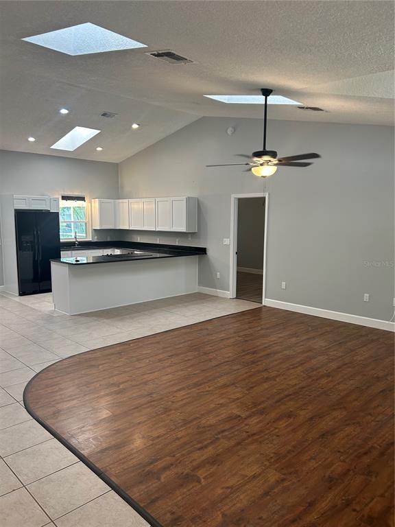 A kitchen with white cabinets and black countertops overlooks a living area with wood flooring — 1181 ANNE ELISA CIRCLE, ST CLOUD, FL