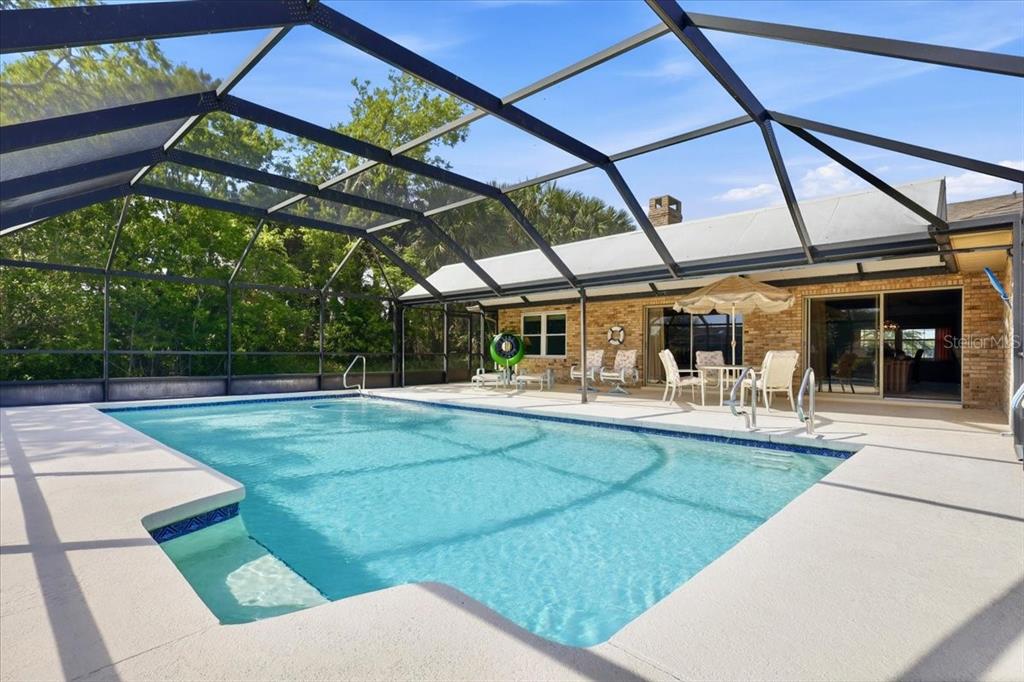 A swimming pool with a screened enclosure sits on a patio behind a brick house — 23 CHRISTOPHER COURT, PALM COAST, FL