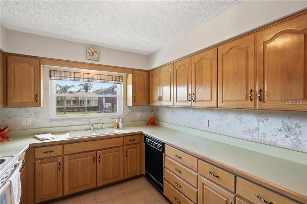 A kitchen features light wood cabinets, a white sink, and floral wallpaper — 23 CHRISTOPHER COURT, PALM COAST, FL
