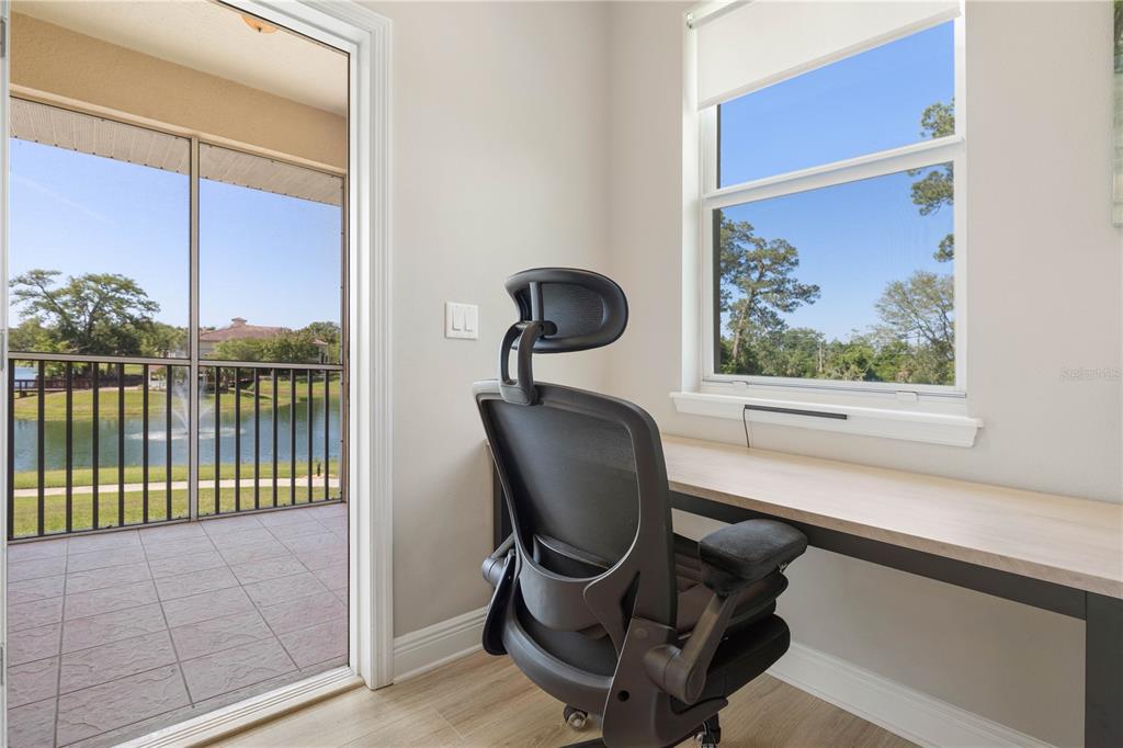 A home office with a desk, ergonomic chair, large window, and a door to a patio — 80 RIVERVIEW BEND S UNIT 821, PALM COAST, FL