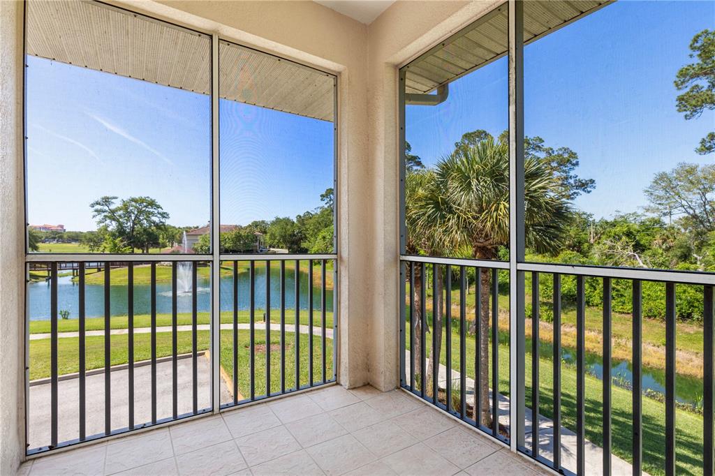 A screened-in balcony with tile flooring overlooks a pond with a fountain and palm trees — 80 RIVERVIEW BEND S UNIT 821, PALM COAST, FL