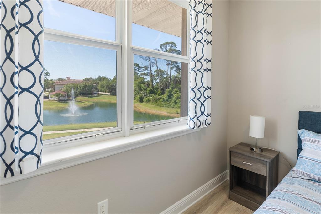 A bedroom window overlooks a pond with a fountain, next to a nightstand and bed — 80 RIVERVIEW BEND S UNIT 821, PALM COAST, FL
