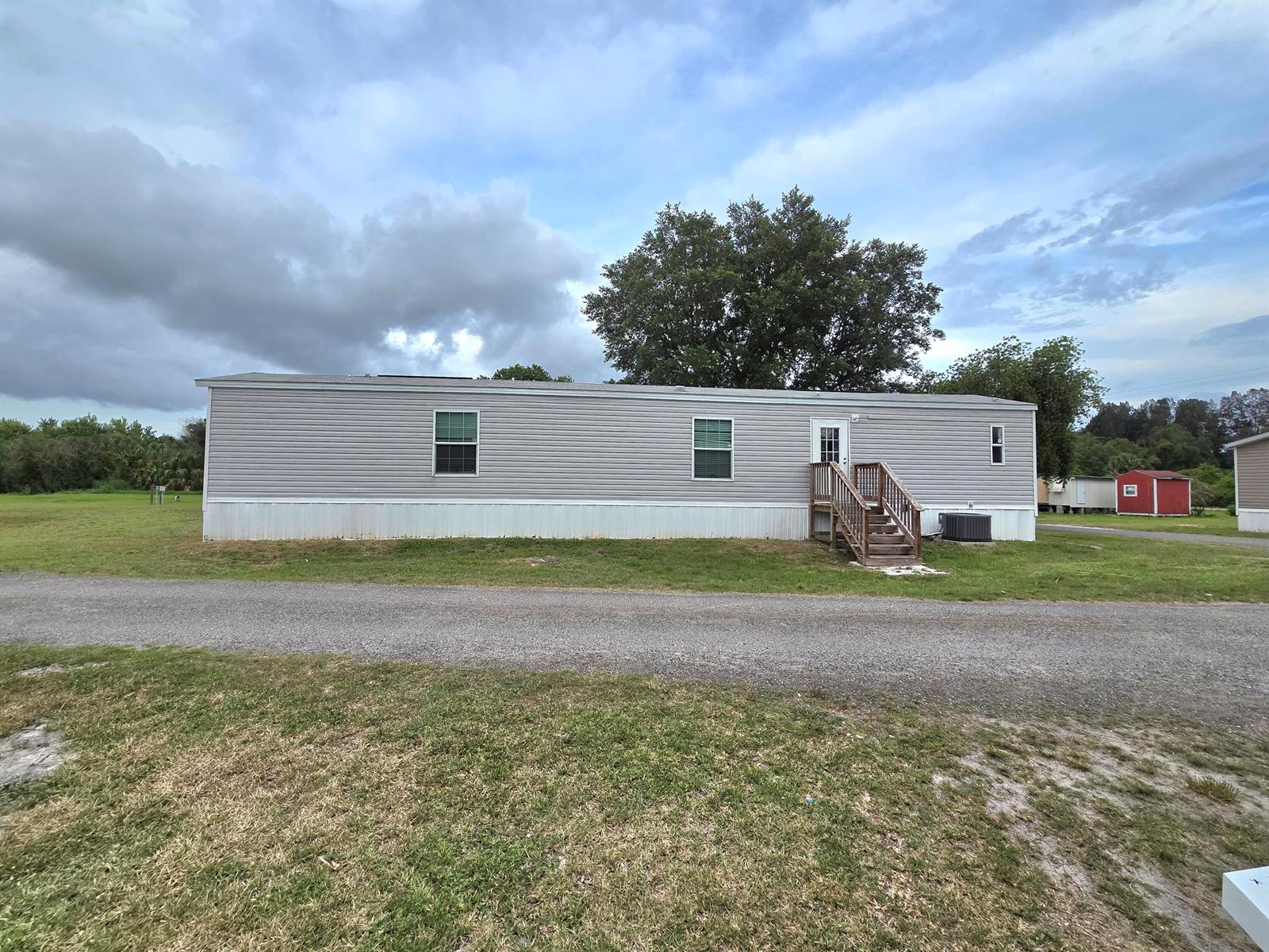 A single-story manufactured home with gray siding sits on a grassy lot near a road — 4649 NW 30th Street, Okeechobee FL 34972, OKEECHOBEE, FL