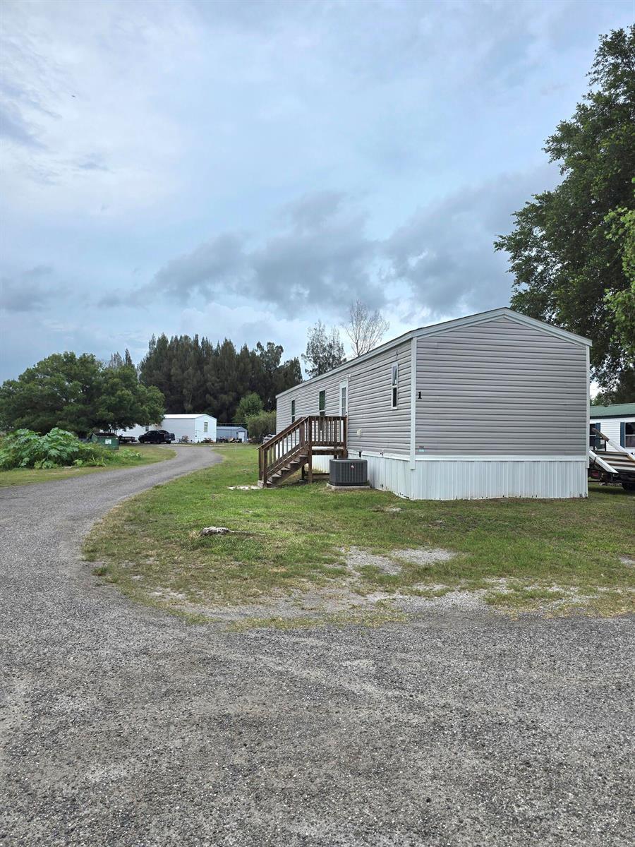 A gray mobile home with a wooden staircase sits on a gravel lot — 4649 NW 30th Street, Okeechobee FL 34972, OKEECHOBEE, FL