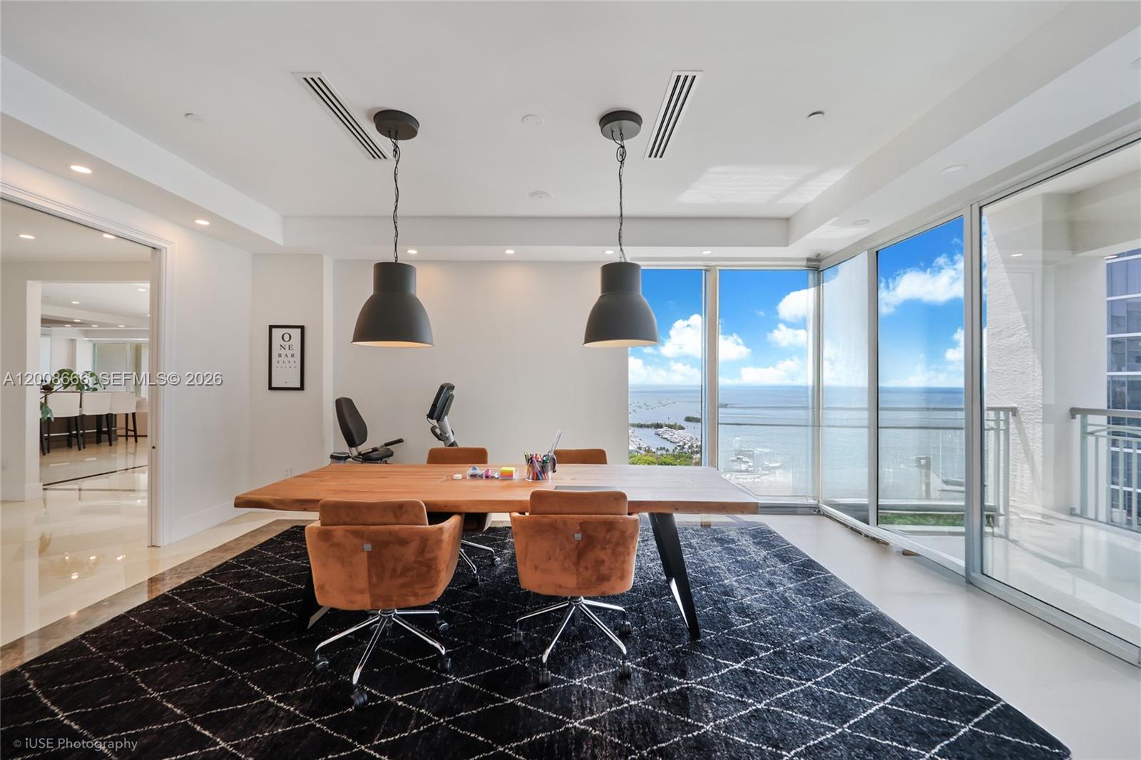 A modern home office features a wooden desk, four chairs, and floor-to-ceiling windows overlooking water — 3400 SW 27th Ave # 2202, Miami FL 33133, MIAMI, FL