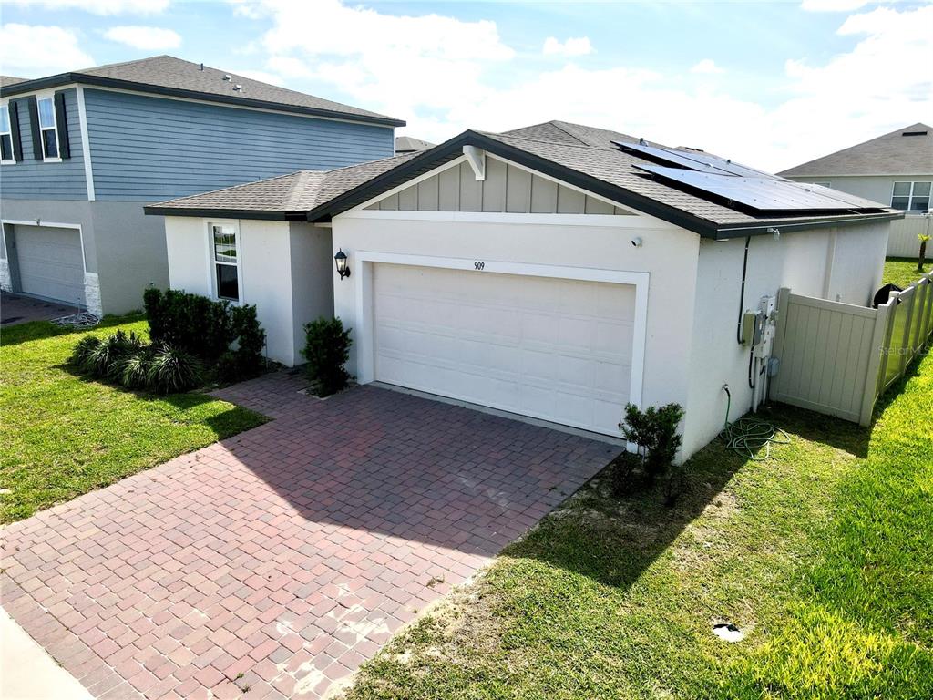 A single-story house with a brick driveway, white stucco walls, and rooftop solar panels — 909 CAMBRIDGE DRIVE, WINTER HAVEN, FL