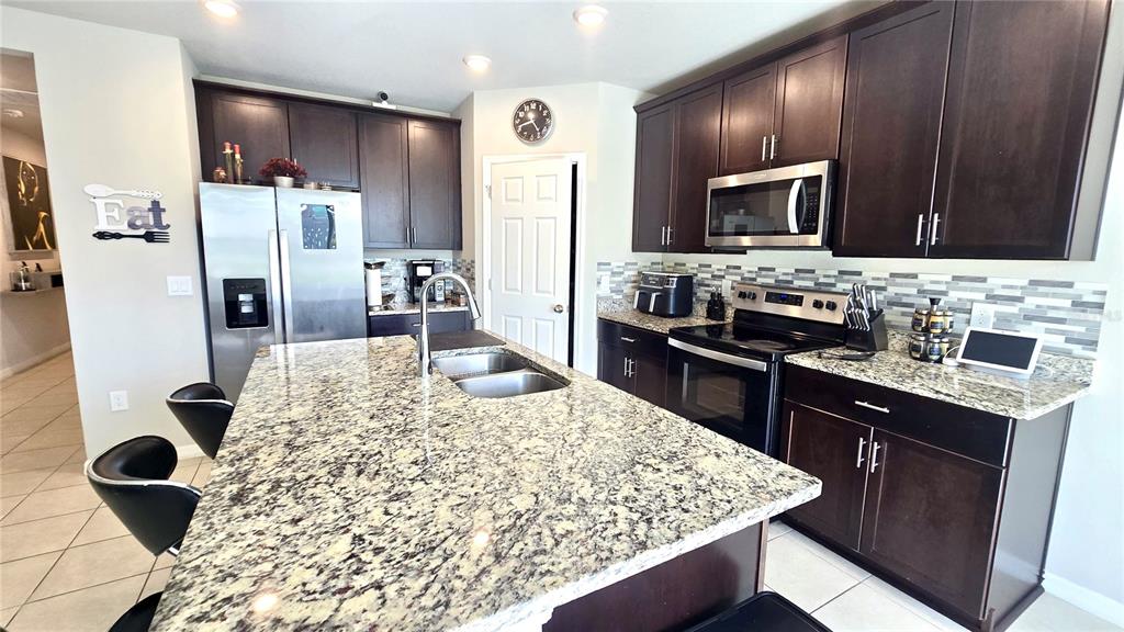 A kitchen features dark wood cabinets, granite countertops, a center island, and stainless steel appliances — 909 CAMBRIDGE DRIVE, WINTER HAVEN, FL