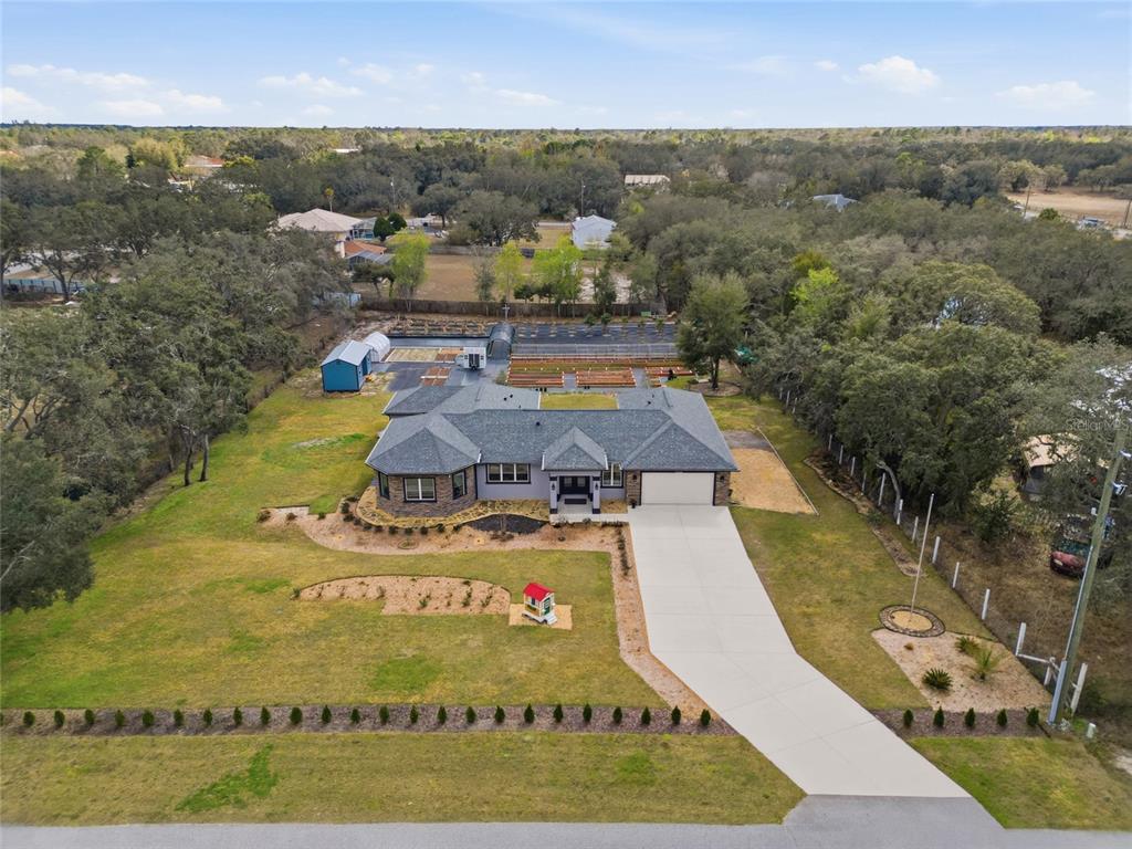An aerial view shows a single-story house with a large driveway and backyard garden beds — 16090 FRINGE TREE DRIVE, SPRING HILL, FL