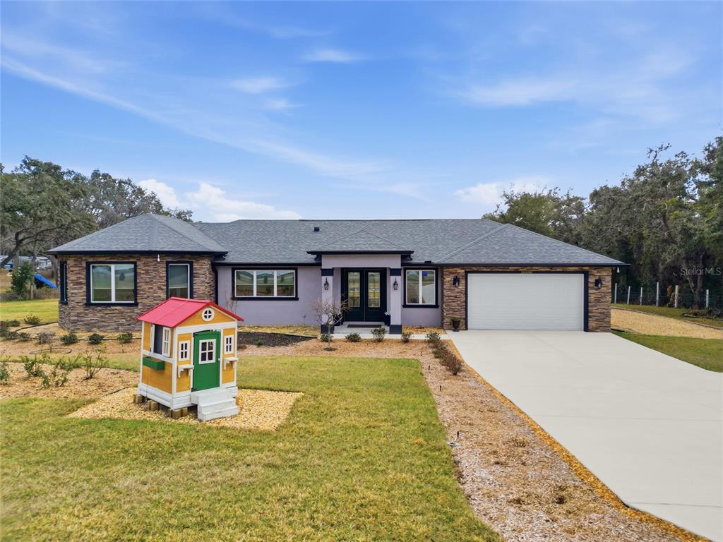 A single-story house with a gray stucco exterior, stone accents, and a front yard playhouse — 16090 FRINGE TREE DRIVE, SPRING HILL, FL