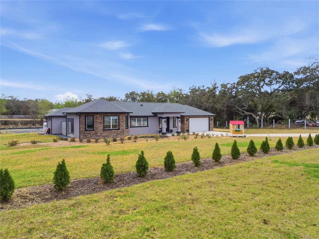 A single-story gray house with stone accents sits on a grassy lot with small trees — 16090 FRINGE TREE DRIVE, SPRING HILL, FL