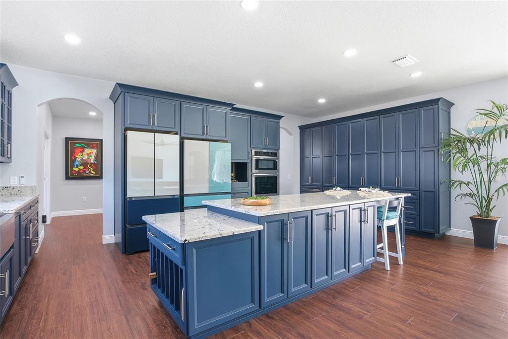 A kitchen features blue cabinetry, a large granite-topped island, and wood-look flooring — 16090 FRINGE TREE DRIVE, SPRING HILL, FL