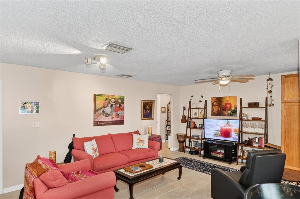 A living room features a red sofa, a black recliner, and shelving flanking a television — 4160 FRUITVILLE ROAD UNIT 11, SARASOTA, FL