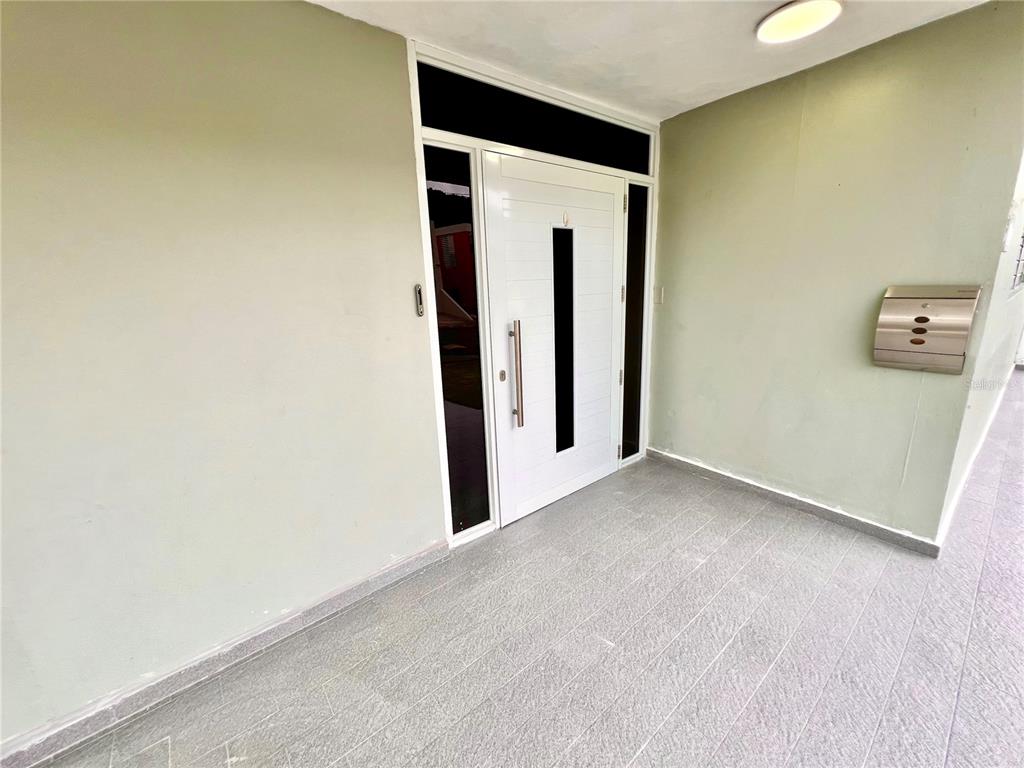 A white front door with black glass accents is set in a light green wall — B8 CALLE 8 LAGO URB ALTAMIRA, FAJARDO, PR