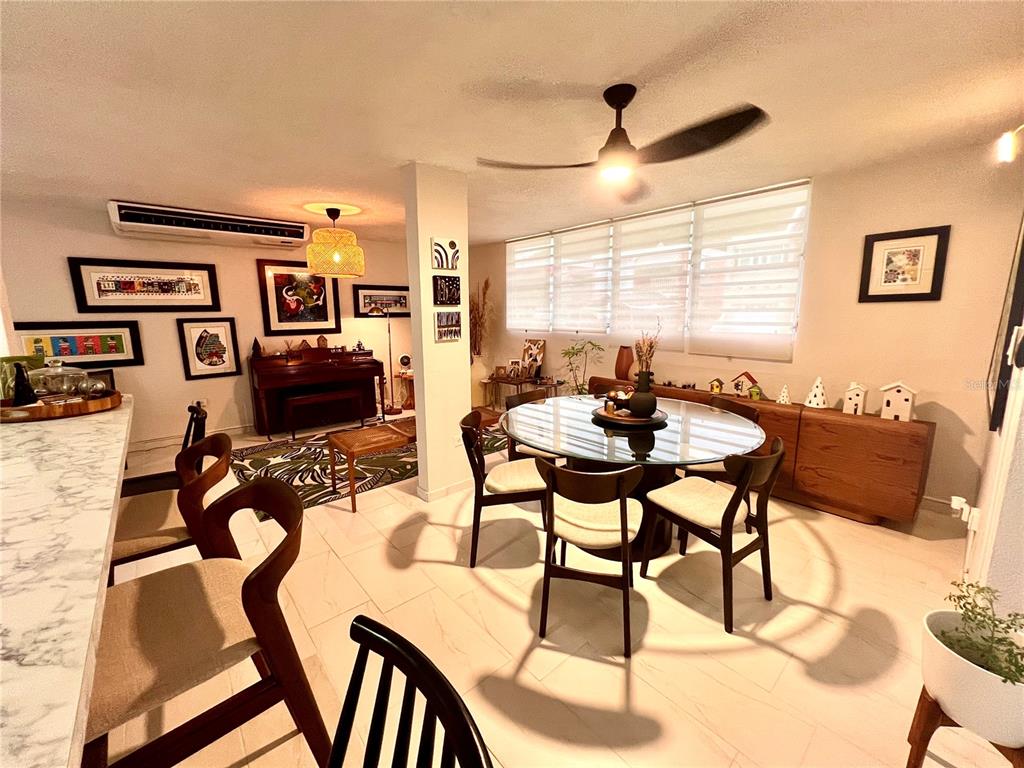A dining area with a glass table, wooden chairs, and a piano in the background — B8 CALLE 8 LAGO URB ALTAMIRA, FAJARDO, PR