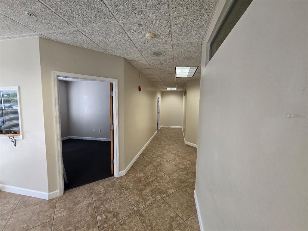 A hallway with tile flooring leads to an open doorway revealing a carpeted office space — 5218 4TH AVENUE CIRCLE E, BRADENTON, FL