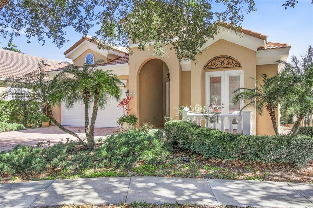 A single-story tan stucco house with a tiled roof, arched entryway, and palm trees — 33 MARSHVIEW LANE, PALM COAST, FL
