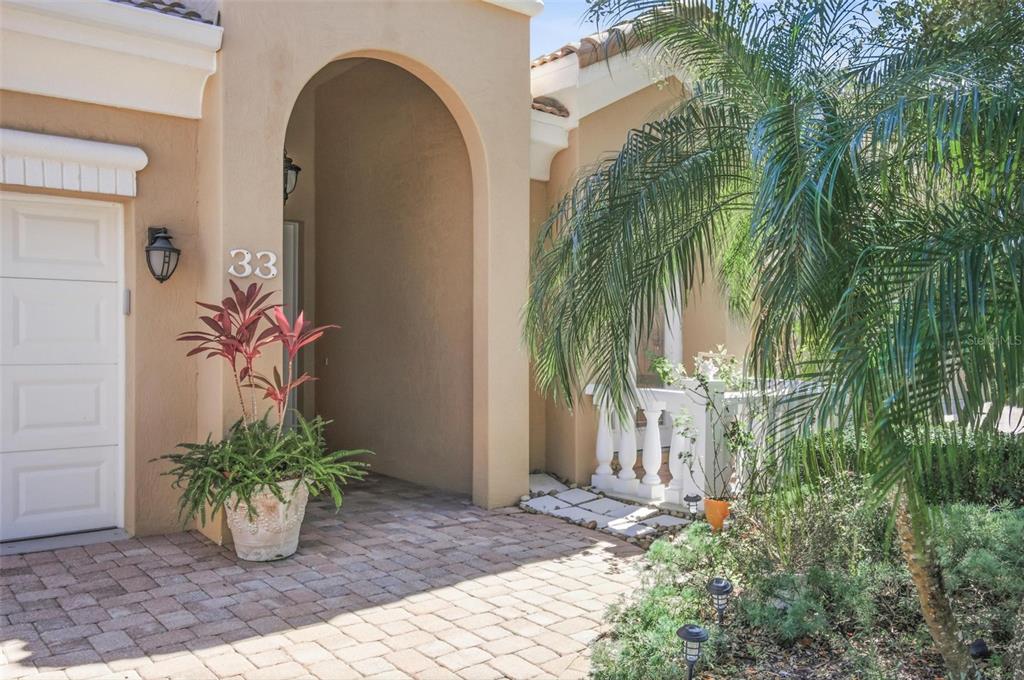 A paved walkway leads to the arched entryway of a tan stucco home with palm trees — 33 MARSHVIEW LANE, PALM COAST, FL